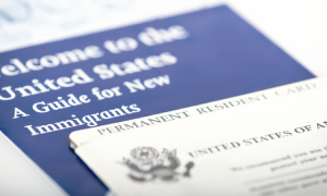 A close-up image of a U.S. Permanent Resident Card (Green Card) partially placed over a blue booklet titled "Welcome to the United States: A Guide for New Immigrants." The image represents immigration-related documents for new U.S. residents.